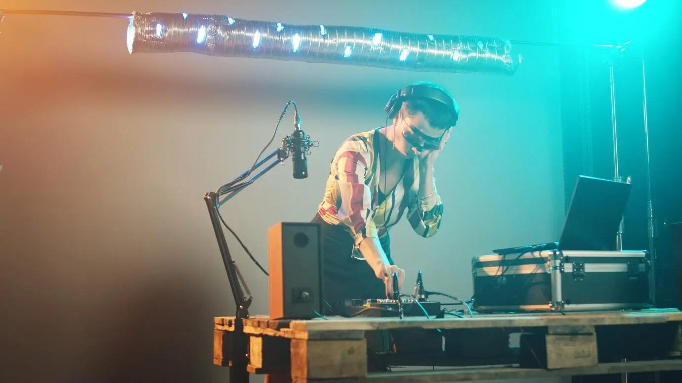 Женщина-артистка на клубной вечеринке микширует звуки на диджейских вертушках, используя аудиоустройства для воспроизведения музыки и создания современного ремикса в стерео, и веселится с диско-оборудованием в ночном клубе. Съёмка с рук.